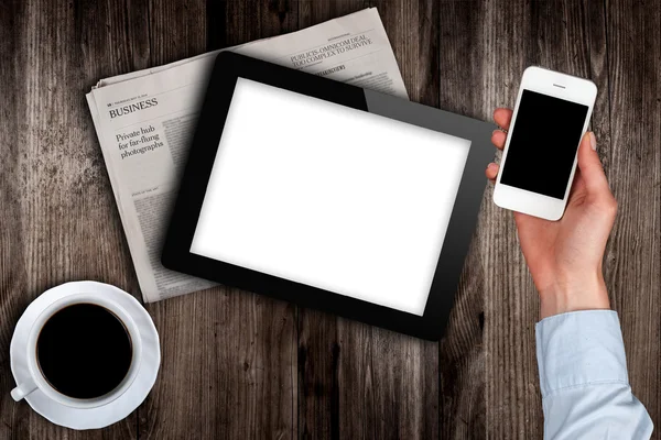 Smartphone in hand and a newspaper with the tablet on the table