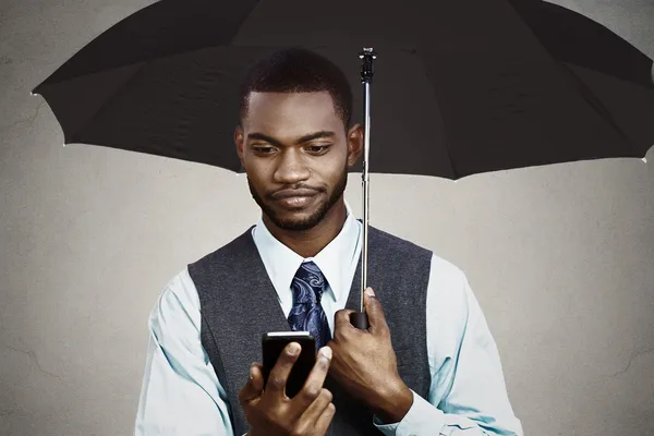 Businessman texting under umbrella