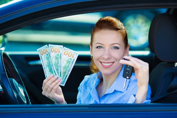 Woman holding car keys, dollar bills, sitting in her new car
