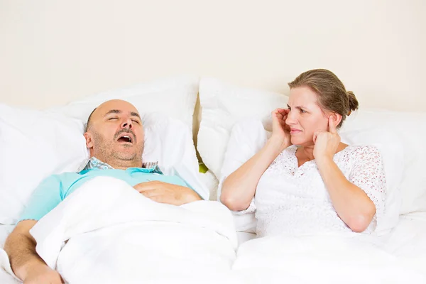 Snoring man, upset woman covering ears, cant sleep.