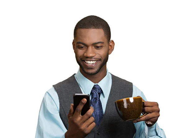 Smiling businessman reading news on mobile and drinking tea
