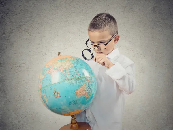 Boy looking at earth globe map through magnifying glass