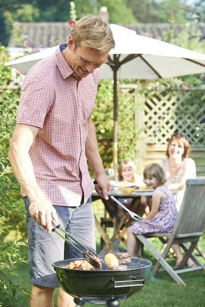 Father Cooking Barbeque For Family In Garden At Home