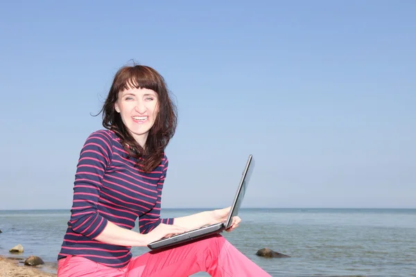 A woman on a sunny beach working on a laptop