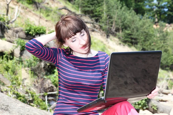 Woman sitting on the trunk of the tree with a laptop