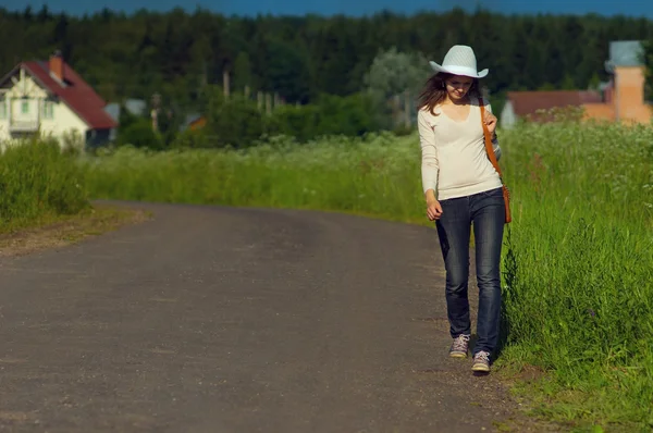 Background girl goes right along countryside road in a cowboy ha