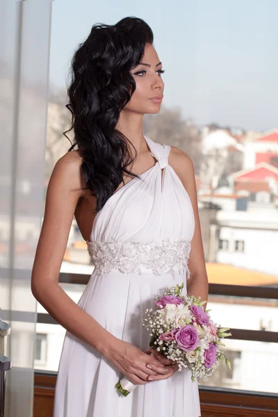 Indoor portrait of adorable bride with black long hair in front of window.