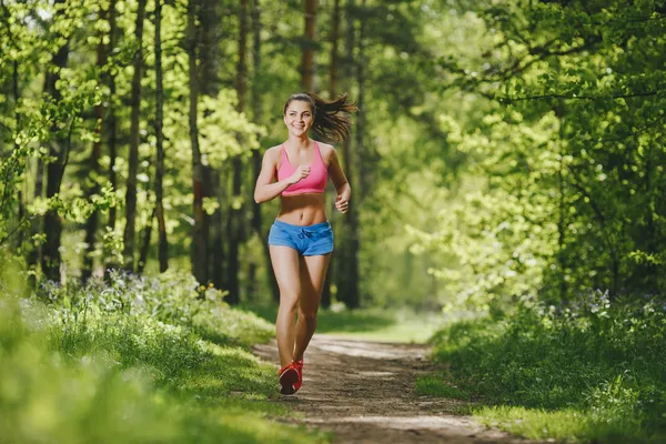 Fitness girl running on forest trail and smiling. beautiful woman runs in park