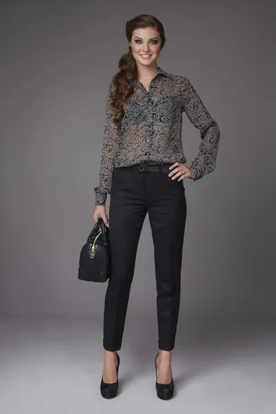 Beautiful sexy young business woman with evening makeup dressed in tight pants silk blouse with lace long sleeves high-heeled shoes and a small black handbag, business clothes for meetings and walks