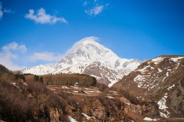 Kazbegi Dağı 'nın aşağısına giden otomobil dağ yolu. Dağın tepesinde kar şapkası.