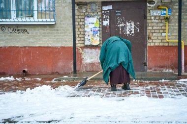 Yaşlı bir büyükanne avlusu girişteki karları temizliyor. Ukrayna, Dnipro - 06.03.2021