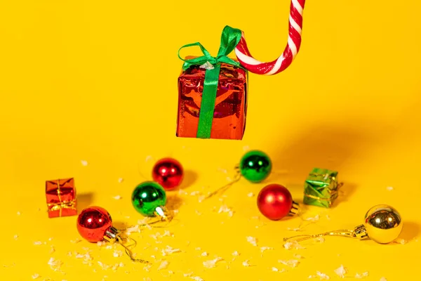 黄色の背景にクリスマスプレゼント付きのギフトボックスを保持しているキャンディー杖ロリポップ 新しい年の装飾のクリスマスお菓子 — ストック写真