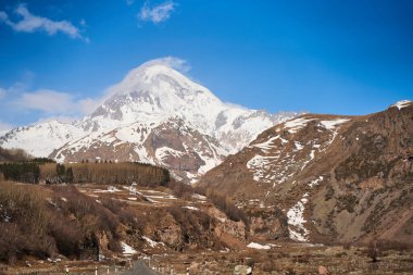 Kazbegi Dağı 'nın aşağısına giden otomobil dağ yolu. Dağın tepesinde kar şapkası.