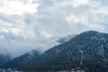 Kış dağı manzarası. Dağlar arasında küçük bir kasaba. Şehrin üzerinde bir bulut asılı..
