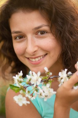 Genç bir esmer kız çiçek açan bir kiraz dalıyla poz veriyor..