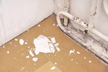 İçerisi tadilata ihtiyacı olan eski bir ev. Duvardan dökülen beyaz alçı, eski radyatörün yanında, yerde yatıyor..