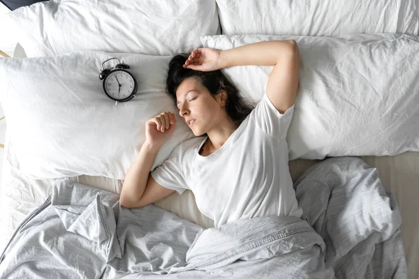 Top view of a girl sleeping next to an alarm clock. Time to wake up. On the wake-up clock 7 a.m. Deep sleep