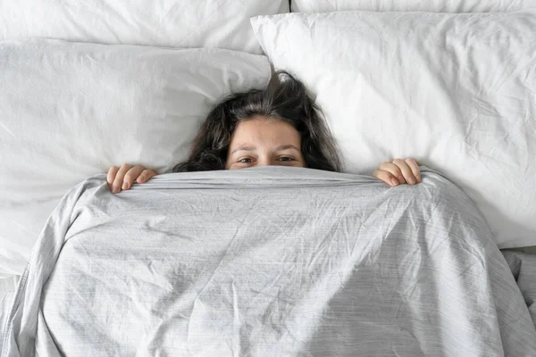 The girl does not want to get out of bed in the morning. Hiding in a blanket. View from above. Ambush in bed.