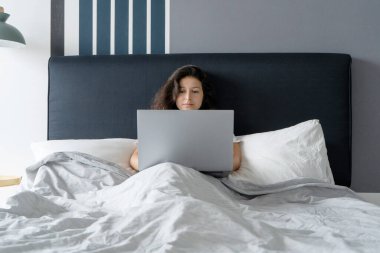 Yatakta dizüstü bilgisayarlı güzel esmer kız. Sabahtan akşama kadar çalış. Elektronik aletler yatmadan önce ya da sabah