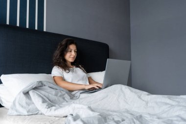Yatakta dizüstü bilgisayarlı güzel esmer kız. Sabahtan akşama kadar çalış. Elektronik aletler yatmadan önce ya da sabah