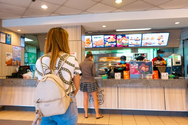 Queue at the cash desk of a fast food restaurant. Masked cashier. People in line keep their distance. Coronavirus pandemic. Langkawi, Malaysia - 06.23.2020