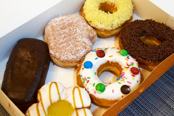 Box of sweets filled with colorful donuts and eclairs.