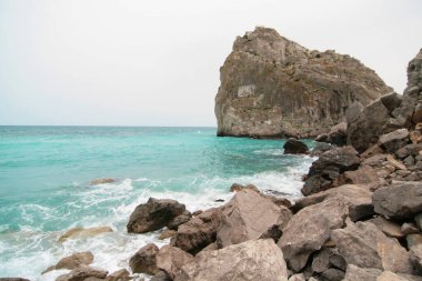 Dalgaların olduğu sahilde büyük bir kaya. Deniz dalgaları kayalara çarpar..