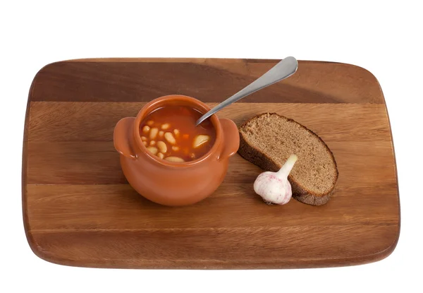 Soup in clay pot with bread and garlic on wooden kitchen board — Stock Photo, Image