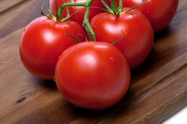 Manojo de tomates frescos con gotas de agua en la tabla de cortar de madera — Foto de Stock