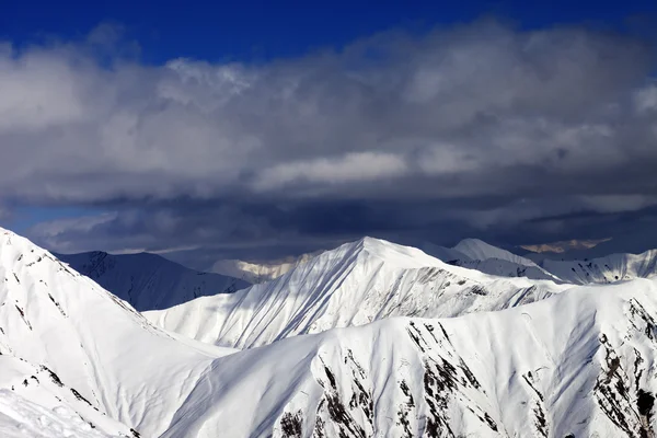 Montañas nevadas iluminada por el sol y cielo nublado — Foto de Stock