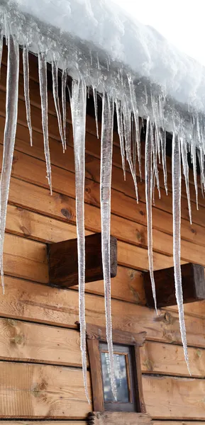 Karla kaplı çatıda büyük buz sarkıtları ile ahşap ev — Stok fotoğraf