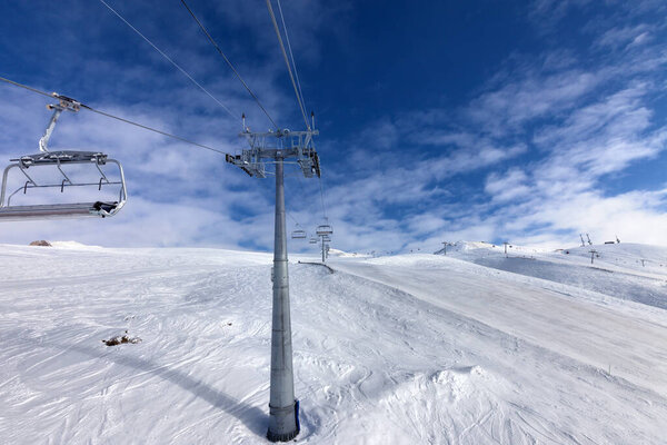 Snowy ski slope, chair-lift on ski resort and blue sky with clouds at wind day. Caucasus Mountains in winter, Georgia, region Gudauri. Wide-angle view.