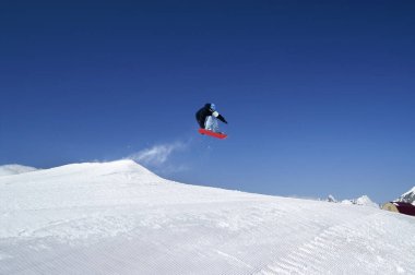 Güneşli kış gününde kayak merkezindeki arazi parkına snowboardcu atladı. Kafkas Dağları, Dombay bölgesi.