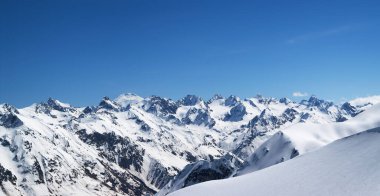 Arka planda Elbrus Dağı ve güneşli soğuk bir günde serbest dolaşmak için karlı yamaçlı karlı dağ manzarası. Kış mevsiminde Dombay ve Kafkasya Dağları 'ndan manzara.