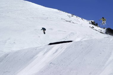 Kar kayakçısı ve kayakçı güneşli kış gününde kar parkında atlıyorlar. Kafkas Dağları, Dombay bölgesi.