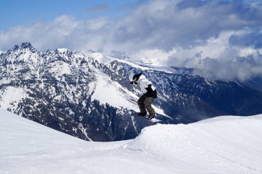 Kış günü kayak merkezindeki kar parkında atlayan snowboardcu. Kafkas Dağları, Dombay bölgesi.