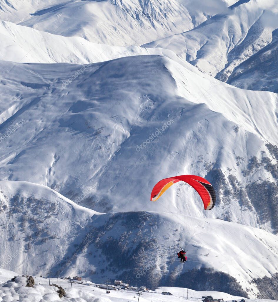 Paragliding at snowy mountains over ski resort at sunny winter day. Caucasus Mountains, Georgia, region Gudauri.