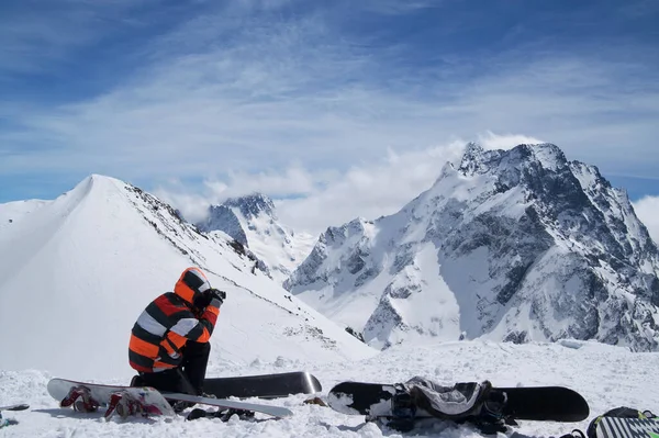 Karlı yamaçlardaki snowboardlar ve snowboardcular yüksek kış dağlarında fotoğraf çekiyorlar. Kafkas Dağları, Dombay bölgesi, Dombay-Ulgen ve Musa Achitara dağları.