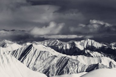 Güneş ışığı karlı dağlar ve gri fırtına bulutları. Kafkasya Dağları, Gürcistan, kışın Gudauri bölgesi. Siyah ve beyaz tonlu manzara.