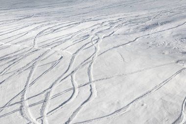 Güneşli kış günlerinde kayak ve snowboard izleri olan karlı bir kayak pisti.