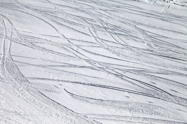 Güneşli kış günlerinde kayak ve snowboard izleriyle tıkalı karlı bir kayak yamacı.