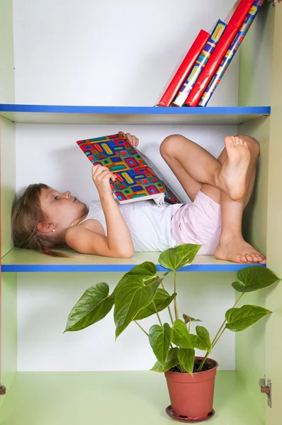 Criança lendo um livro em uma estante — Fotografia de Stock