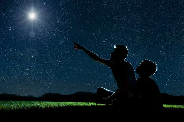 爸爸和儿子晚上坐在草地上 看着圣诞节的夜空 — 图库照片