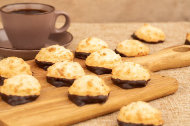 Kahverengi tahta üzerinde hindistan cevizi kurabiyeleri ve çuval bezinde bir fincan kahve..