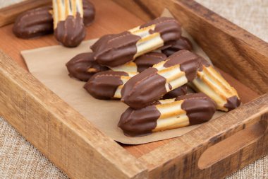 Kahverengi ahşap kutuda çikolatalı kurabiyeler bej renkli çuval bezi arka planda. Yan yatay görünüm.