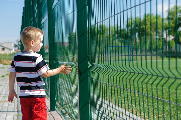 Kleine jongen permanent in de buurt van raster hek — Stockfoto