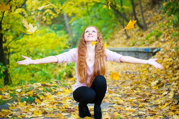 Roodharige meisje gooien bladeren in de herfst park — Stockfoto