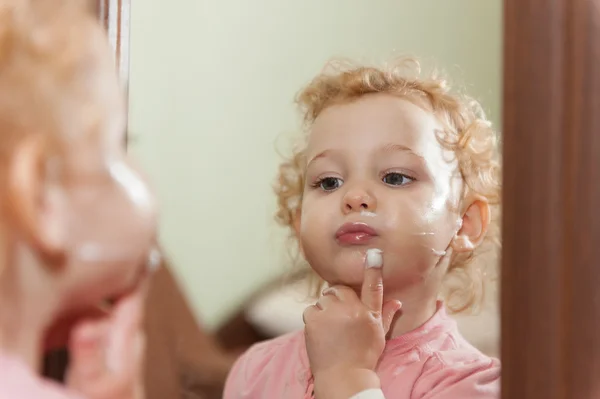 Söt baby tillämpa kräm på hennes kinder — Stockfoto