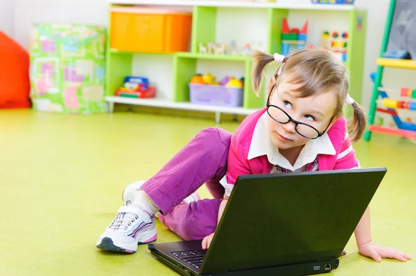 Carino bambina in occhiali con computer portatile sul pavimento — Foto Stock