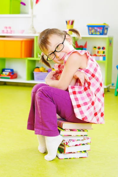 Cute little girl in eyeglasses sitting on stack of books — Stock Photo, Image